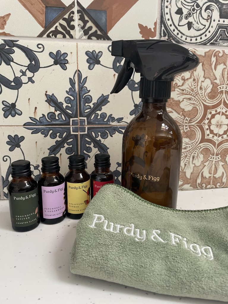 Purdy & Fig's bottle for life with four cleaning concentrate bottles sitting on a white worktop next to a green cloth
