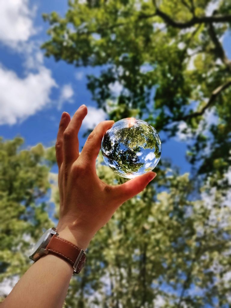Eco-friendly household products. Hand holding a glass ball reflecting the sky and trees