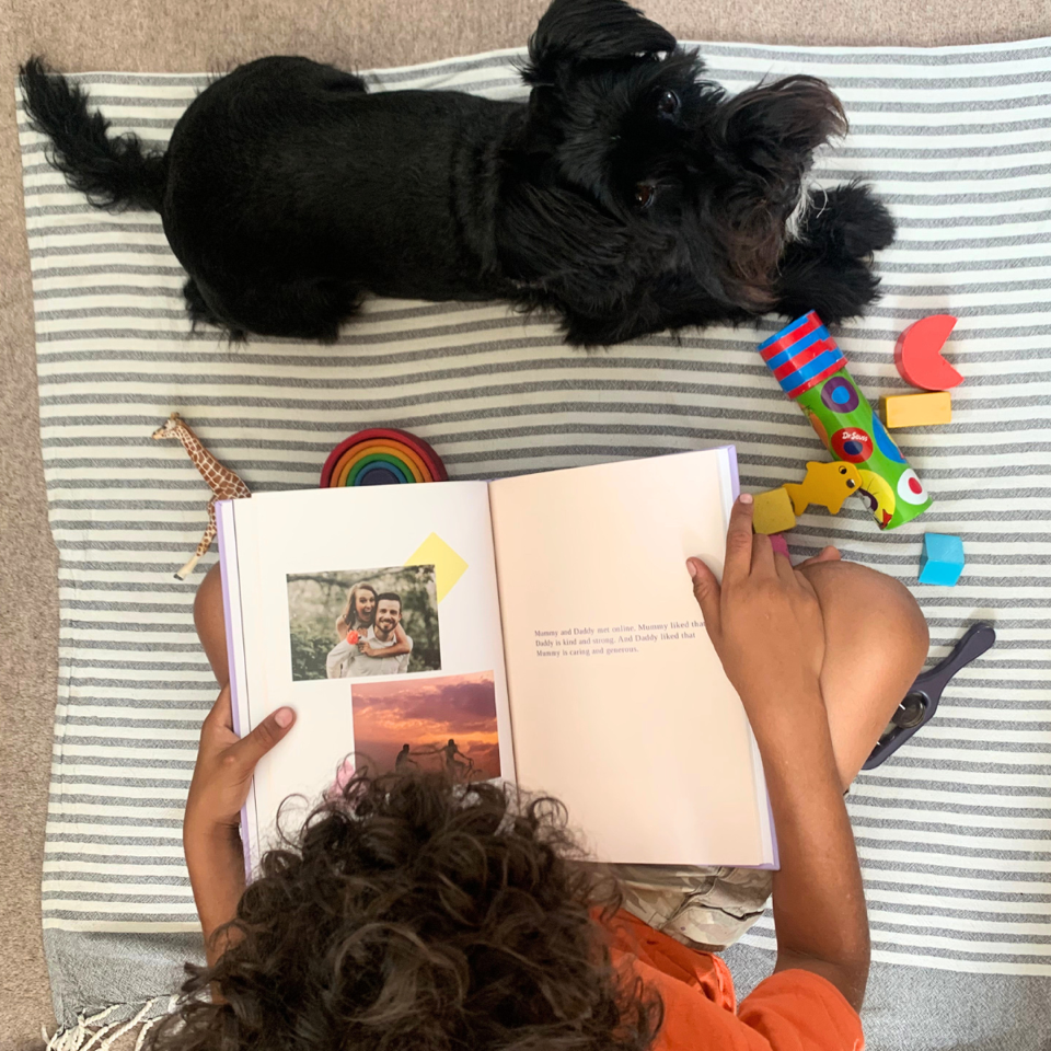 Ariel shot of a child looking at a StoryDo book, resting on a play mat with a small black dog beside them, looking up at the camera