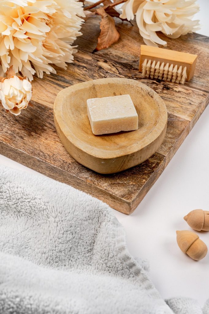 Wooden board with a soap dish, nail brush and loofah with a white towel in the foreground