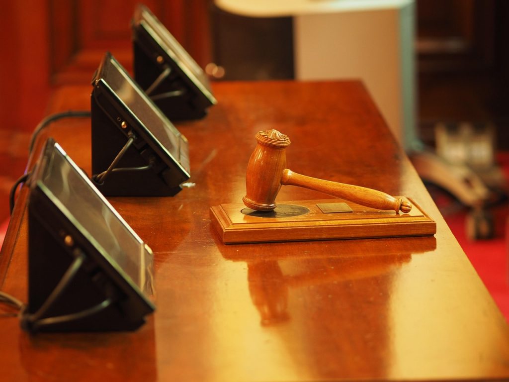 A judge's desk in a courtroom with a gavel and 3 screens