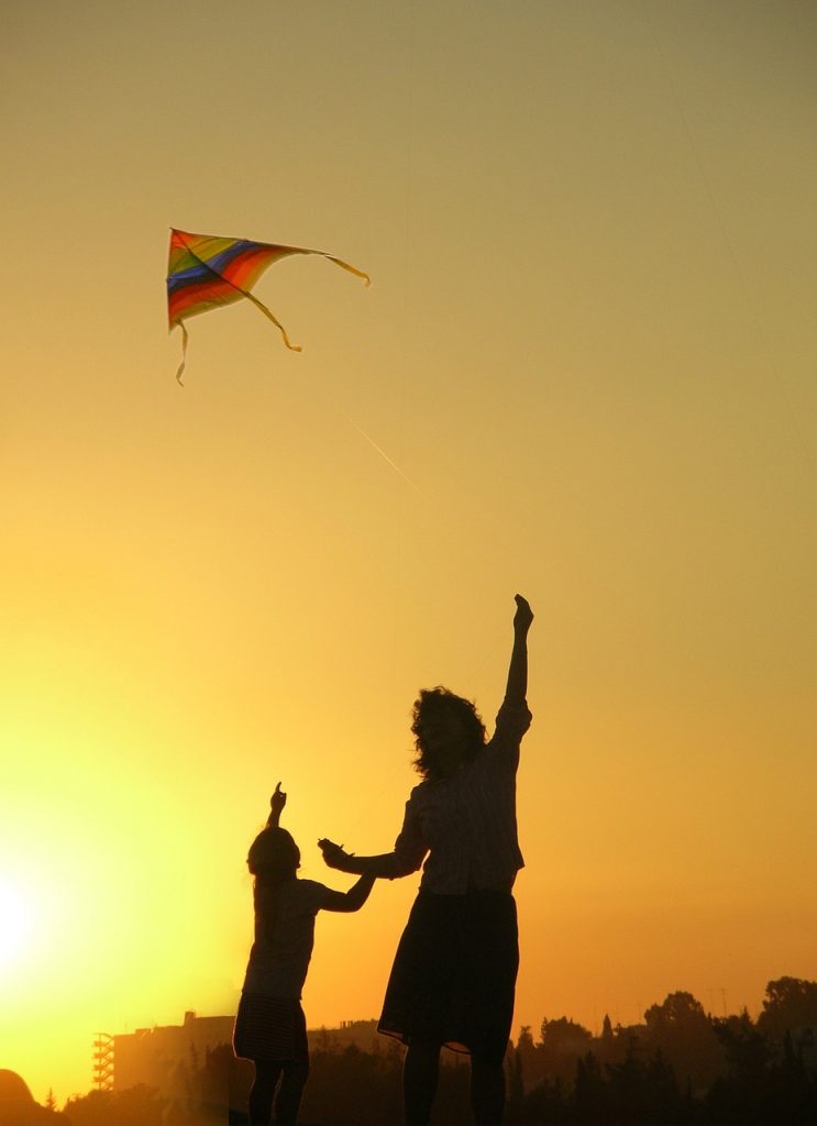 Silhouette of a parent and child flying a kite against an orange sky showing mindfulness parenting and connection