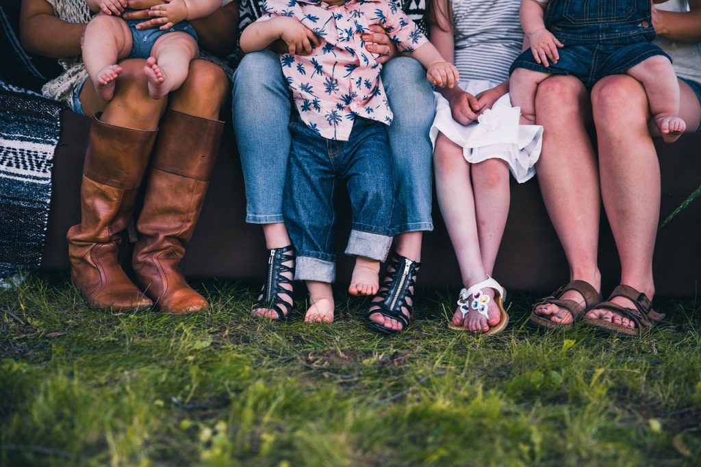 A mixture of adult and children's legs sitting on a bench outside