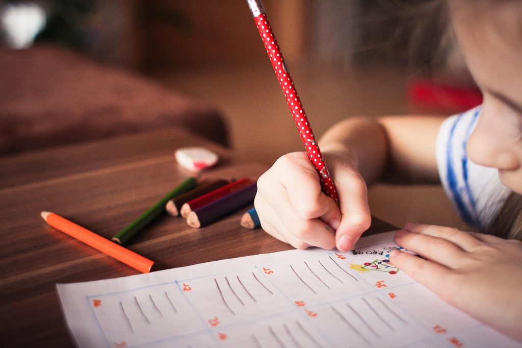A child's hand writing on a page with a pencil, supporting adopted children in school