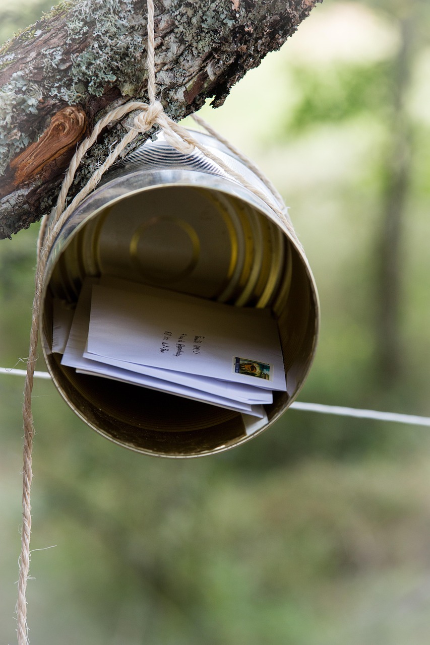 A metal can hanging from a branch with string with several sealed envelopes inside