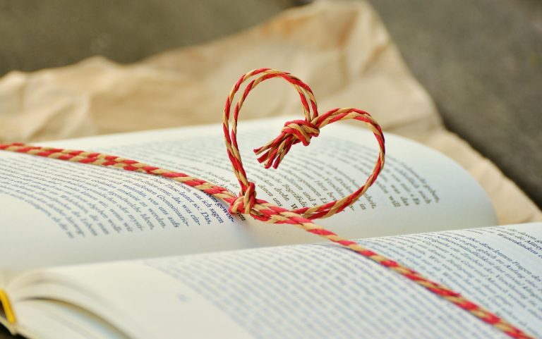 A piece of red string tied into a heart shape across an open book