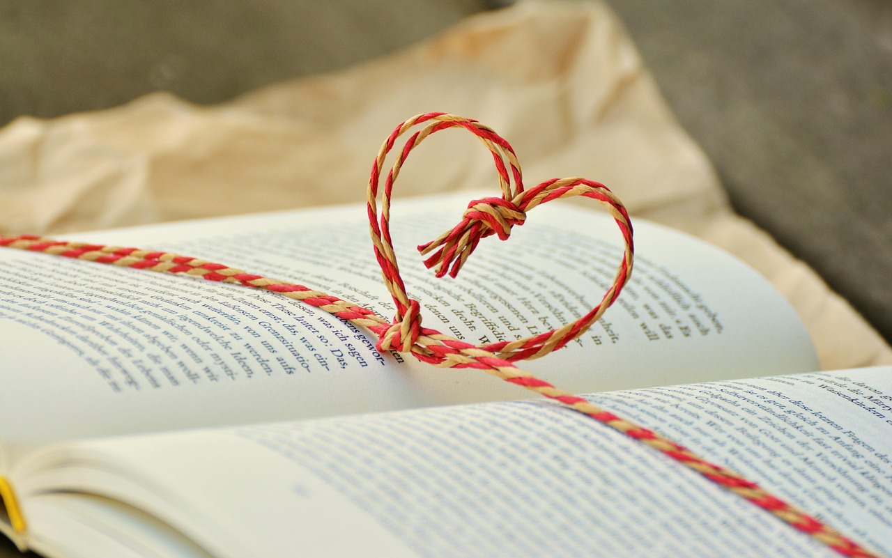 A piece of red string tied into a heart shape across an open book