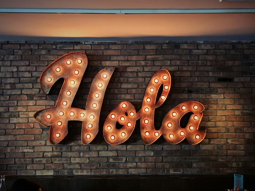 The word "Hola" written in lights against a brick wall, representing the benefits of bilingualism for children