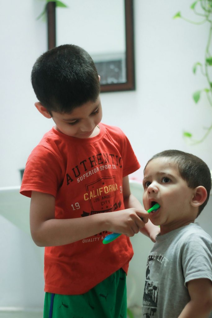 An older boy brushing the teeth of a younger boy showing tips for making teeth brushing fun for your kids