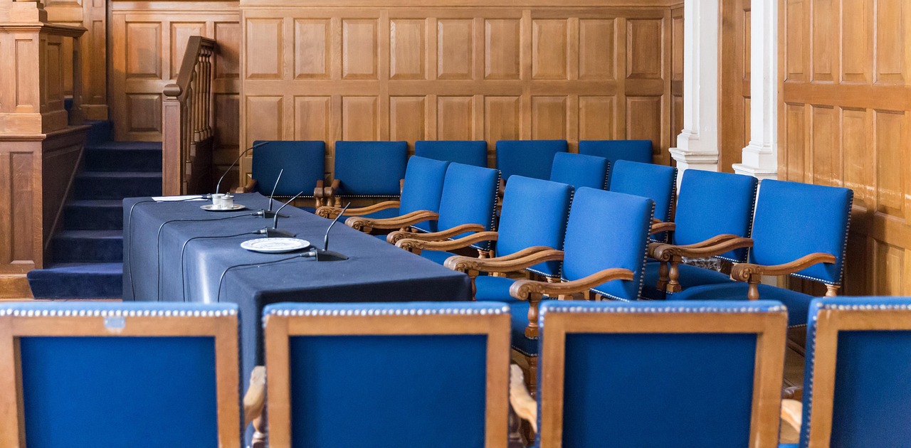 A courtroom with wooden panelled walls and blue chairs