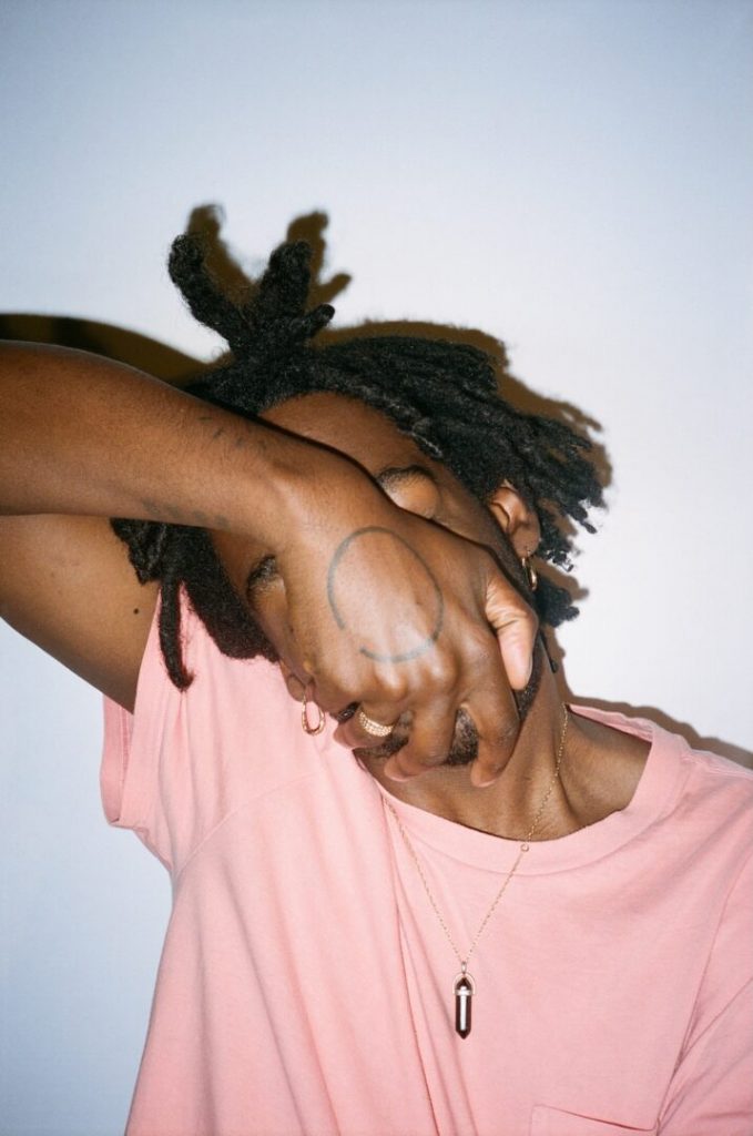 Image of Marley Starskey-Butler with their hand over their face, wearing a pink t-shirt