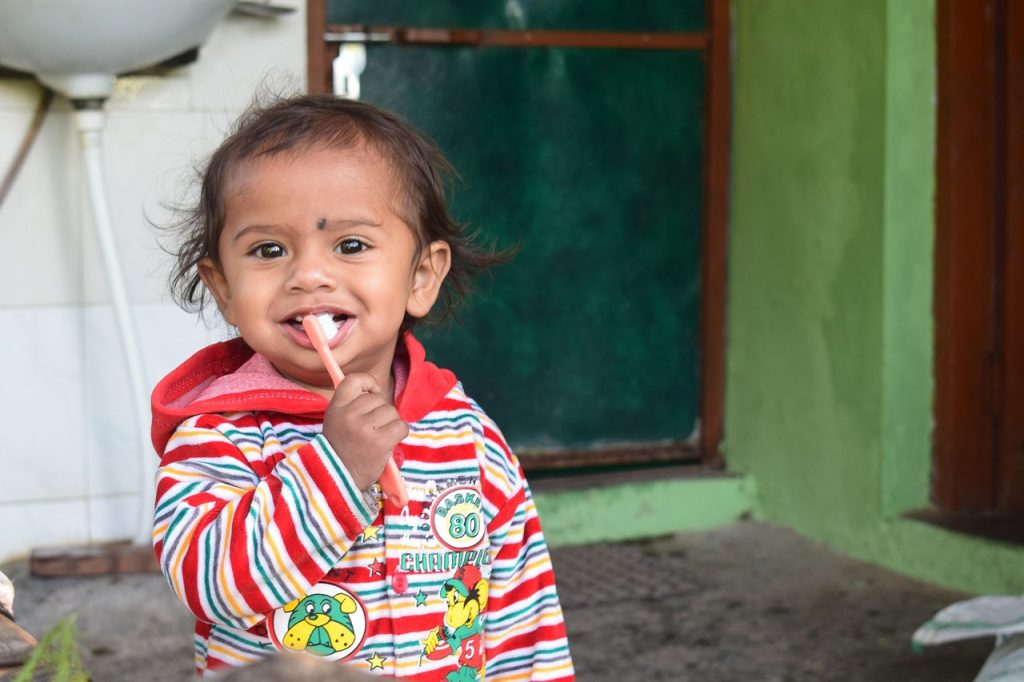 Young child wearing a stripy coat brushing their teeth standing in front of a sink