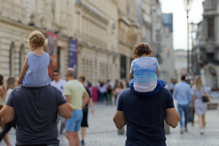 People walking away from the camera along a street with two men carrying young children on their shoulders
