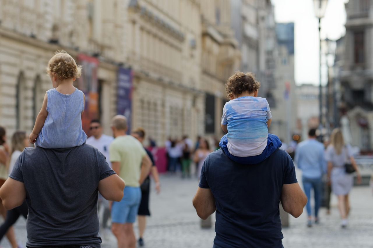 People walking away from the camera along a street with two men carrying young children on their shoulders