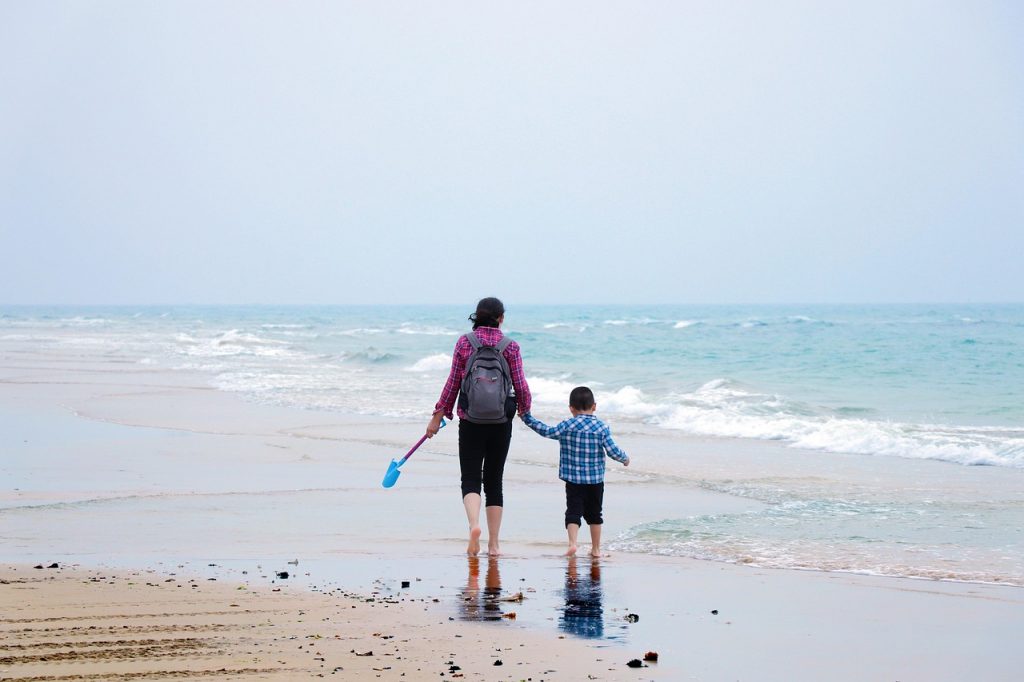 A mother and son holding hands, walking along a beach walking away from the camera showing the benefits of a family-first business