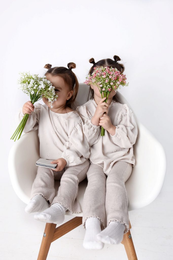Two children sitting on a chair holding a bunch of flowers each in front of their faces, showing how photographing children safely can be done