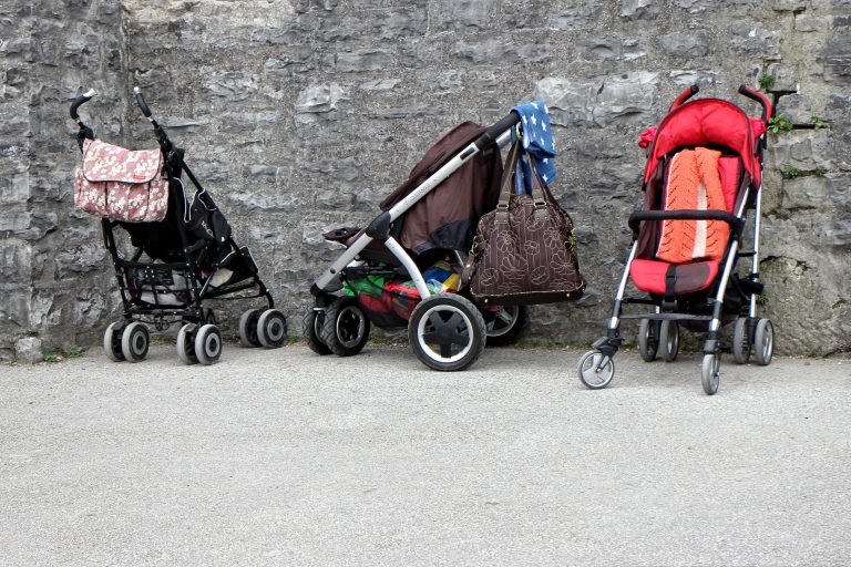 Three baby strollers side by side in front of a wall