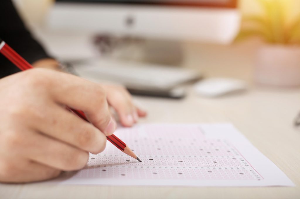 A child's hand holding a pencil marking an exam sheet