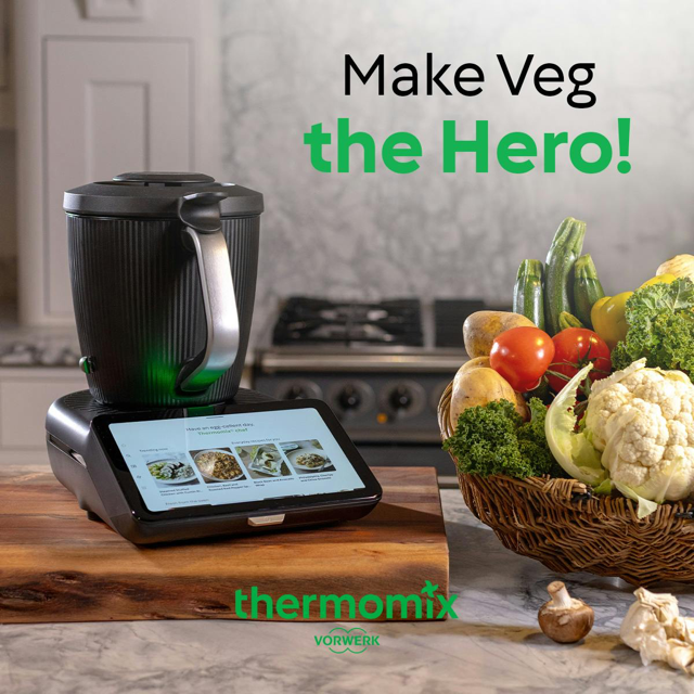 Thermomix kitchen appliance on a wooden board surrounded my fresh vegetables