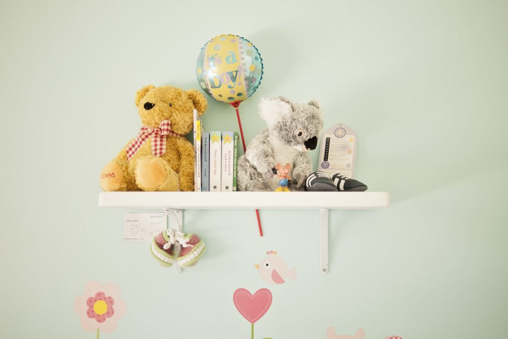 A white shelf on a white wall with children's toys and books to show that renting your baby kit is one option for new parents