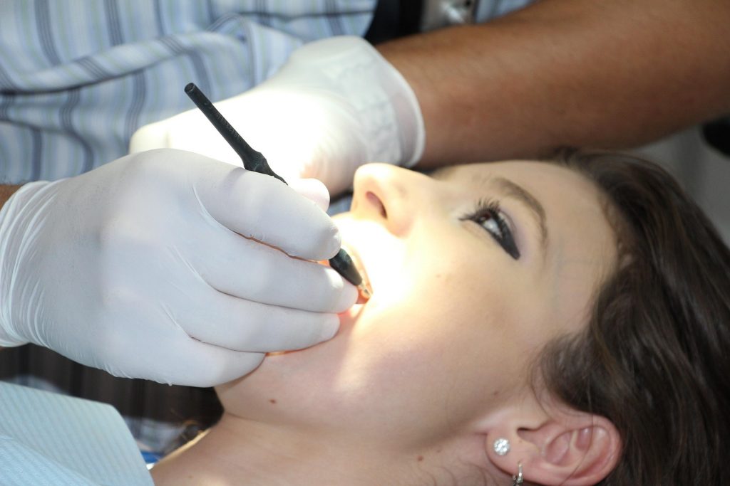 A woman with her mouth open and a dentist looking at her teeth using a dental instrument