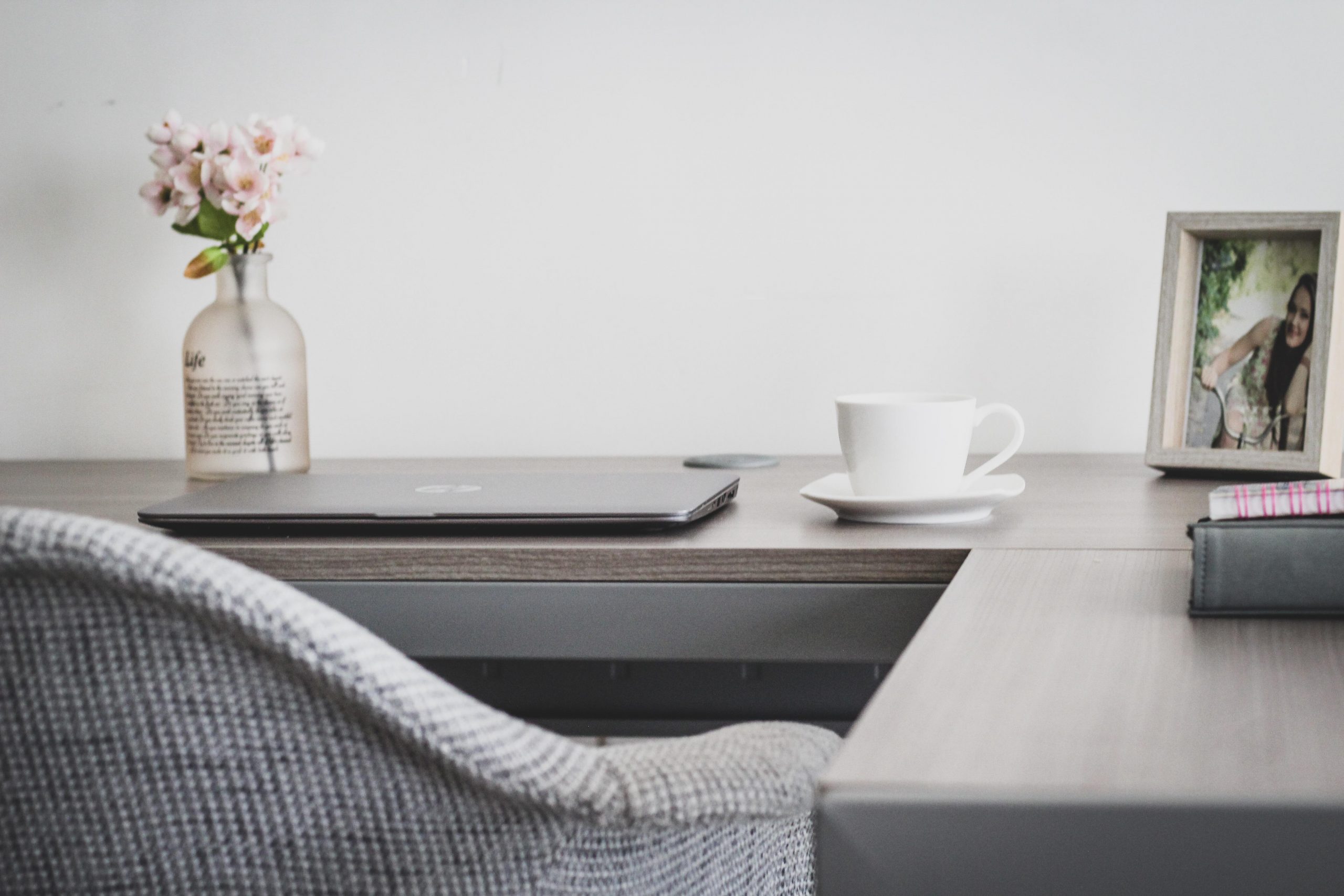 A corner desk with a closed laptop on it, cup and saucer, flowers in a jar and desk chair pushed against the desk representing menopause in the workplace