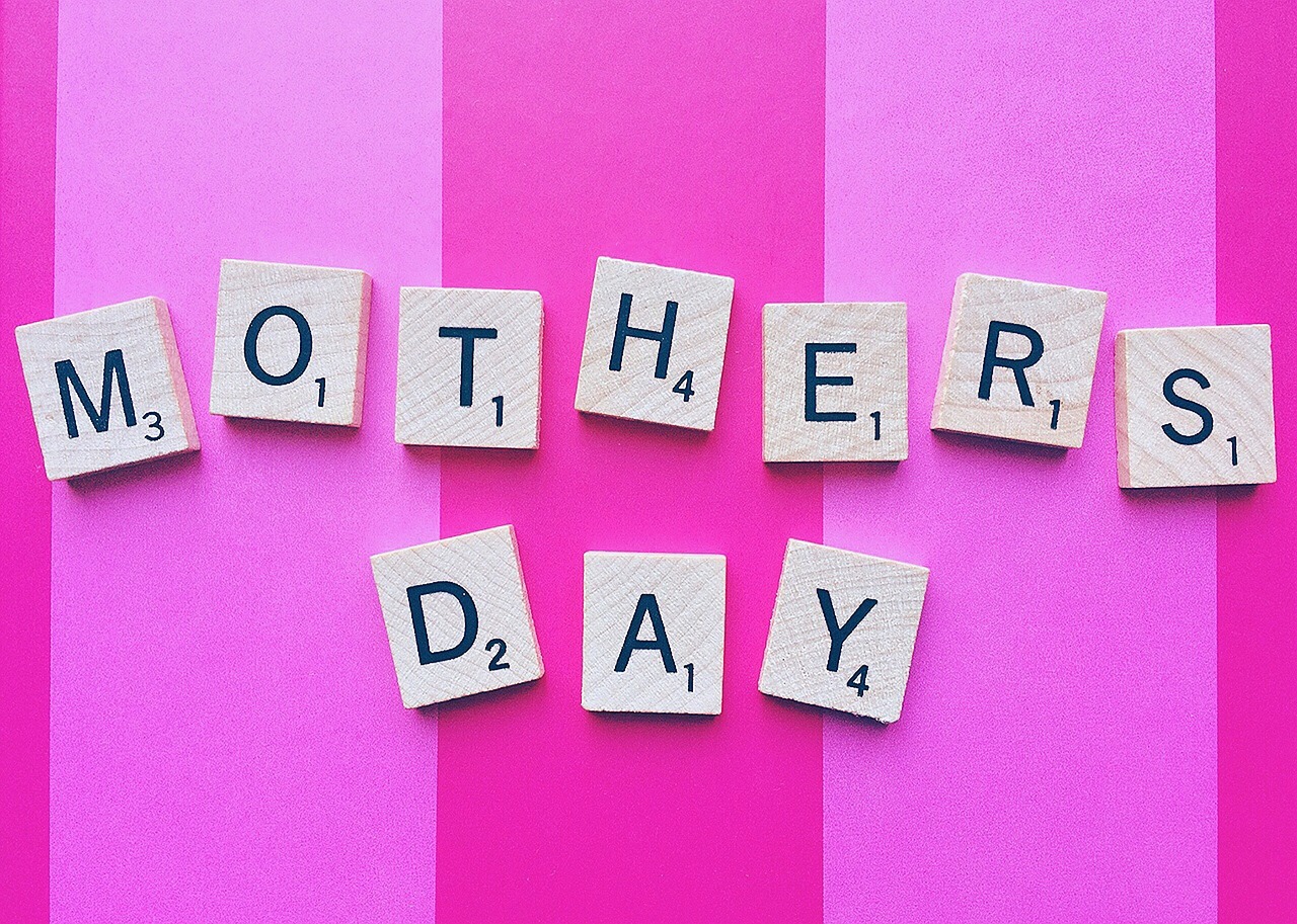 Scrabble tiles spelling Mother's Day against a pink striped background