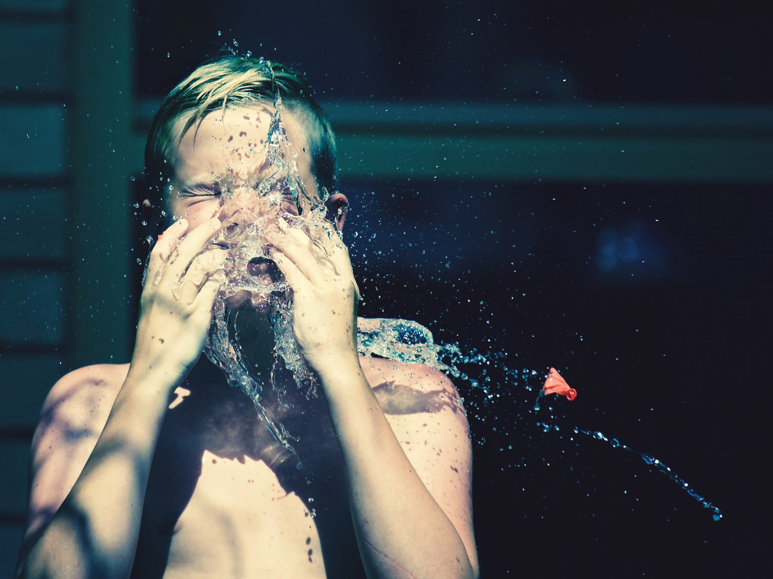 A child splashing their face with water against a black background
