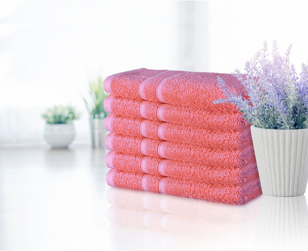 A pile of pink towels with white pots of purple flowers beside them, resting on a white table