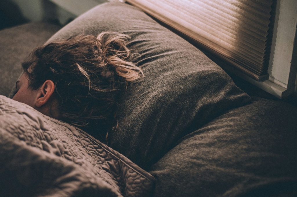 A woman sleeping in a bed with grey cover and pillow showing the result of wellness tips for a good night's sleep