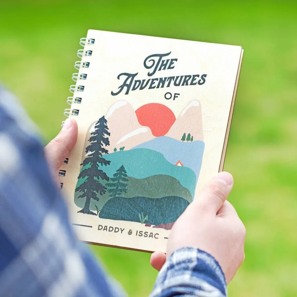 Front cover of Oakdene Design's wooden Father's Daybook featuring a man holding the book which has a mountain design on the front.