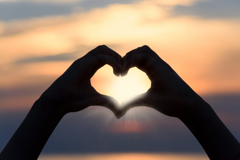 A pair of hands making a heart shape against a backdrop of a sunset