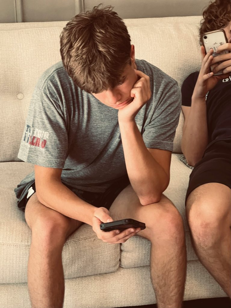 Teenage boy looking at his phone which relates to the question is your teen's screen habit affecting their eyesight