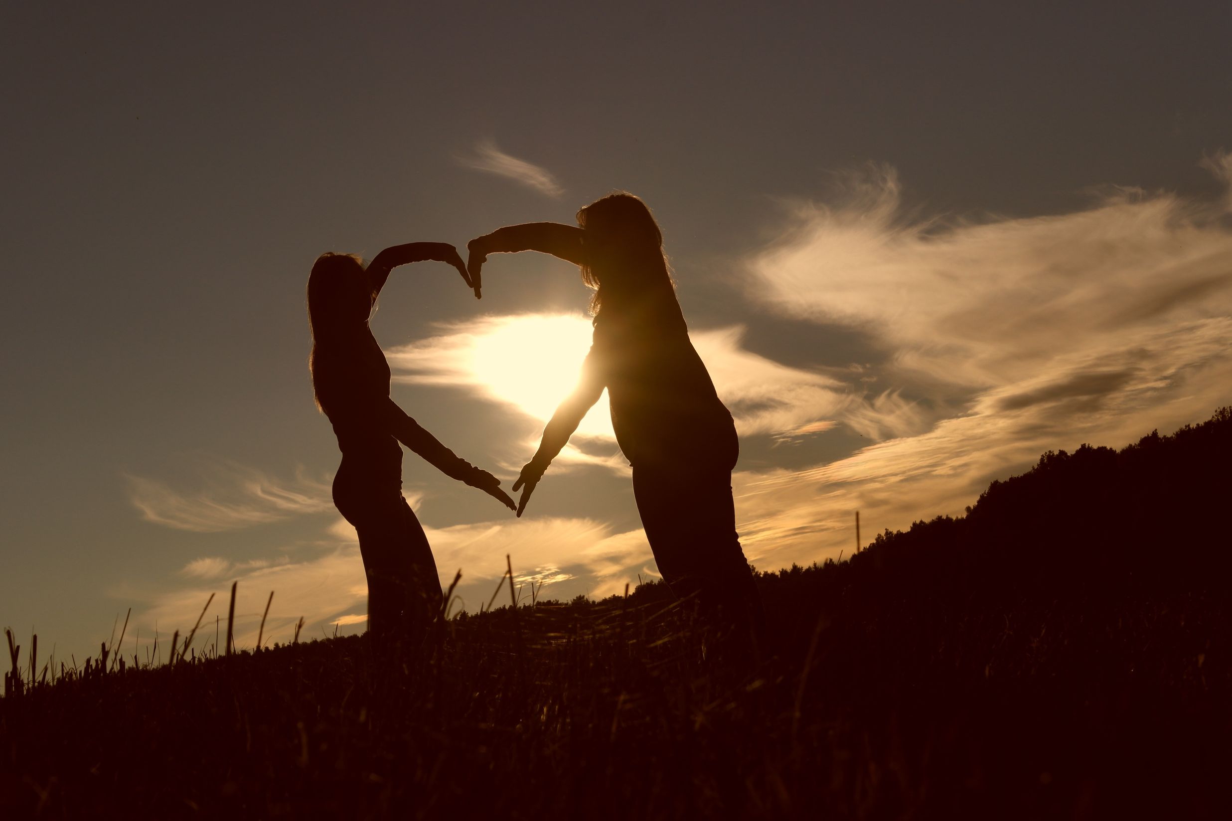 Silhouette of two people creating a heart shape with their arms against a sunset