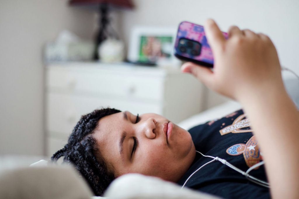 A teenager lying on a bed looking at their mobile phone