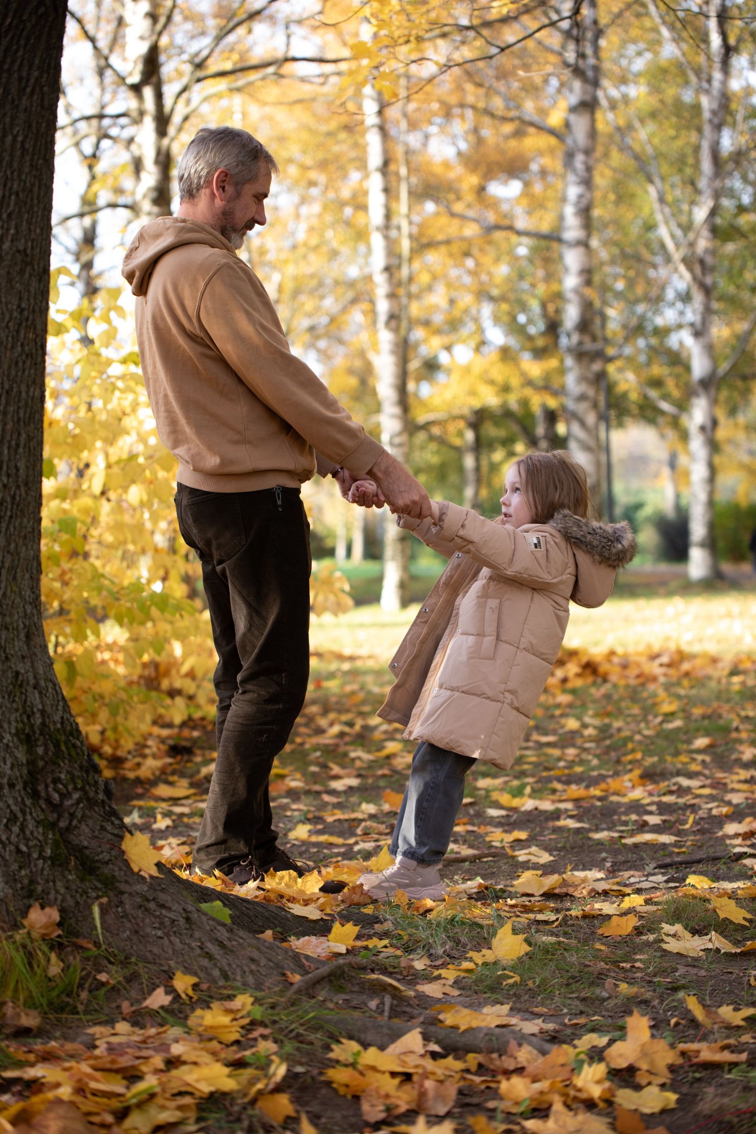 A father and son holding hands facing each other in an autumnal wood, representing the path to fatherhood