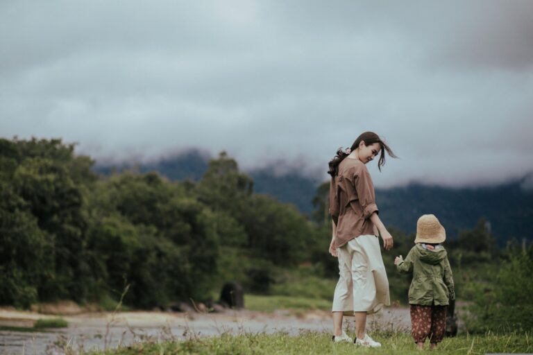 A mother and young daughter holding hands against a backdrop of trees